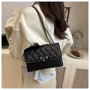 Detail of a black quilted chain bag with silver lock worn by a model in a modern home setting
