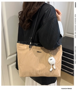 Detail of khaki pleated tote bag with black trim and plush charm worn by model