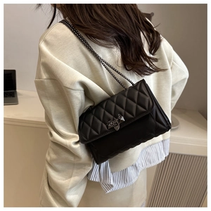 Detail of black quilted chain bag worn crossbody with silver studs and metal charms