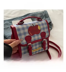 Detail of blue plaid crossbody bag featuring red apple print and yellow brand label