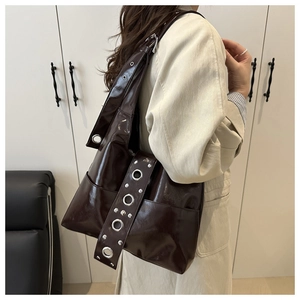 Detail of dark brown tote bag with glossy finish and silver eyelet metal studs