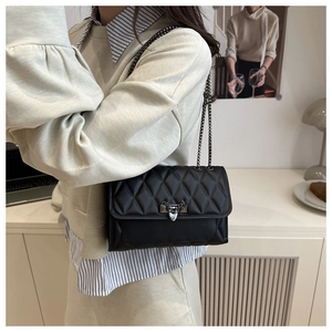 Close-up of black quilted shoulder bag with silver V-clasp and studded chain strap