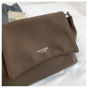 Detailed macro view of dark brown matte leather bag with elegant fashion text on white bedding