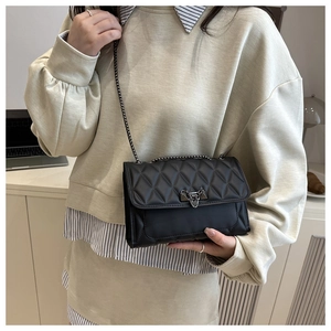 Detail of black quilted crossbody bag featuring metal chain strap and twist-lock closure