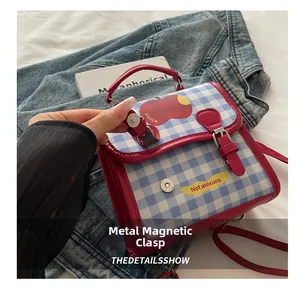 Detail of the magnetic clasp on a blue plaid crossbody bag with a red apple pattern