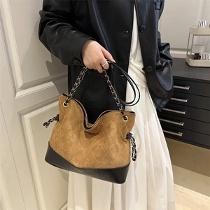 Quilted brown suede tote bag with metal chain strap carried by a woman in a leather jacket