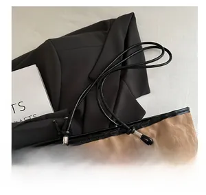 Detail of a brown tote bag with pleated texture and a decorative white fluffy keychain