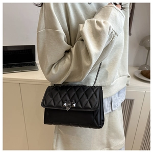 Close-up of black quilted leather shoulder bag with chain strap in a modern office setting
