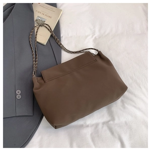 Brown leather shoulder bag with metal chain strap displayed with blazer and magazine