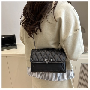 Rear view of model wearing a black quilted chain bag with metal lock and stud details
