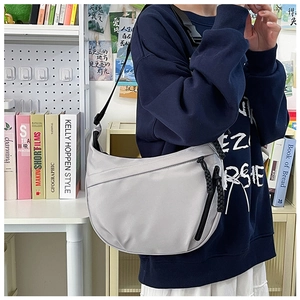 Close-up of light gray nylon crescent bag with woven zipper details on a model