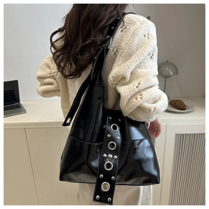 Close-up of black patent leather tote bag with silver grommets and rivet details