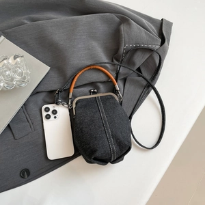 Vintage denim bucket bag with kiss-lock closure and leather handle on a grey blazer background