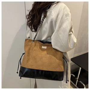 Detail of suede tote bag with chain strap and metallic hardware in a minimalist setting