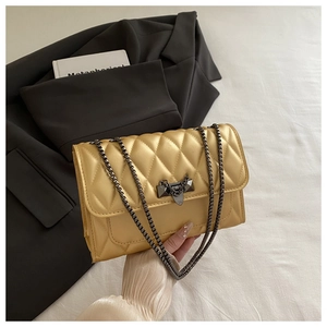 Detail of golden quilted crossbody bag with metal chain strap and luxury lock clasp