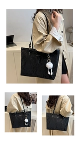 Detail of black pleated tote bag featuring a plush white charm and slender shoulder straps