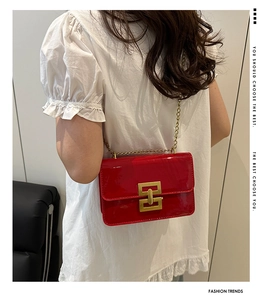 Detail of red patent leather crossbody bag with golden chain and geometric lock on white dress