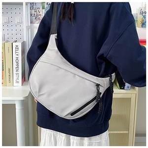 Light gray crescent nylon bag with adjustable strap worn as a crossbody in a home setting