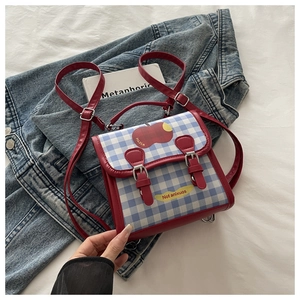 Détail du sac à dos à carreaux bleus avec bordure en cuir rouge et motif pomme