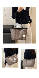 Detail of silver textured tote bag with cute white plush monster pendant and metal logo