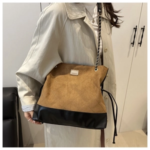 Detail of vintage quilted bucket bag with chain strap and tassel on brown suede