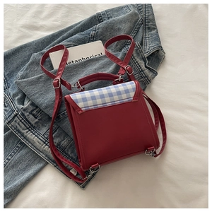 Detail of red backpack featuring blue and white plaid flap with silver metal buckle lock