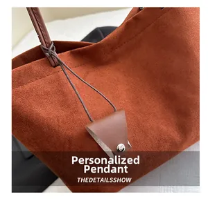 Macro shot of dark brown suede tote bag featuring a leather charm and metal buckle