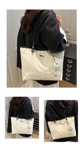Detail of white tote bag with black straps, metal logo, and plush monster charm