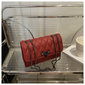 Detail of red quilted crossbody bag featuring metal chain and V-shaped lock closure