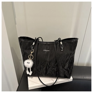 Detail of black wrinkled texture tote bag with silver logo and white plush charm