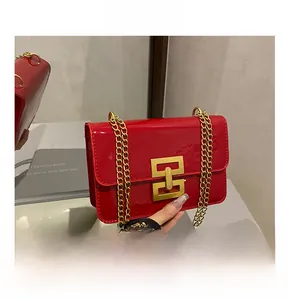 Detail of red patent leather crossbody bag with gold chain and geometric clasp