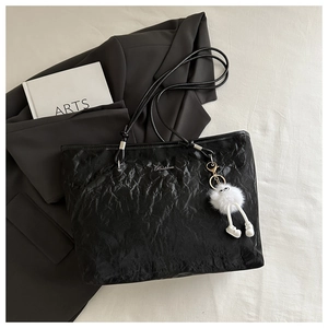 Detail of black pleated tote bag with plush charm on a minimalist urban setting background