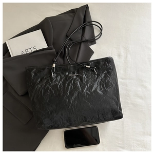 Close-up of black tote bag with wrinkled texture, metal logo and slim shoulder straps