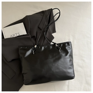 Detail of a black matte tote bag with thin shoulder straps and silver metal hardware accents