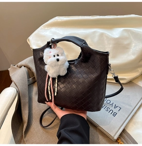 Close-up detail of dark brown woven leather handbag featuring a white fluffy dog charm