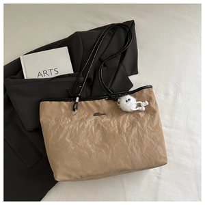 Detail of khaki pleated tote bag with black straps and a cute plush charm accessory