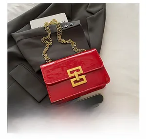 Detail view of red patent leather crossbody bag with gold buckle and chain strap