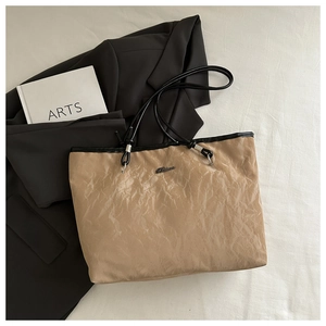 Close-up of beige tote bag with crinkled texture, black handles, and metallic logo detail