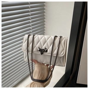 Close-up of white quilted chain bag featuring a unique gunmetal bow-shaped lock