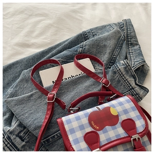 Détail du sac à carreaux rouge et bleu avec motif pomme et bandoulières en cuir rouge