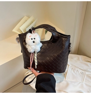 Detail of dark brown woven leather handbag with a plush puppy charm on a clean background
