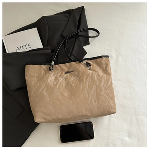 Detail of khakhi tote bag featuring pleated texture and black contrast shoulder straps