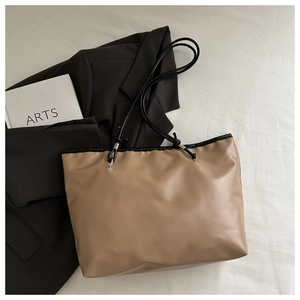 Detail of khaki tote bag with black handles next to a book and black blazer
