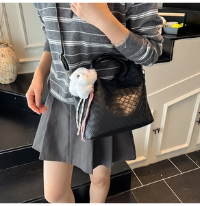 Detail of black woven leather tote bag with plush bunny charm on a shoulder strap