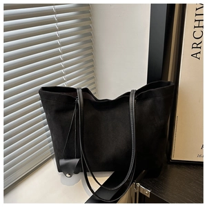 Close-up of black matte tote bag with thin shoulder straps and leather charm by a window