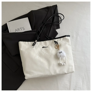 Minimalist white tote bag with black handles and a cute plush monster charm