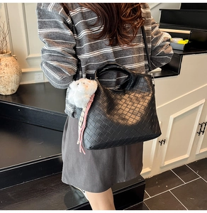 Detail of black woven crossbody bag with cute plush animal charm and adjustable strap
