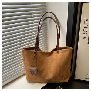 Detail of a brown suede tote bag with a small leather charm in a natural light setting