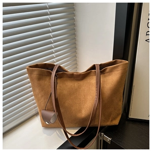 Brown suede tote bag with long handles and heart pendant leaning against a white ledge