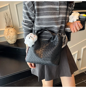 Detail of black woven bucket bag with long leather strap and cute plush puppy charm